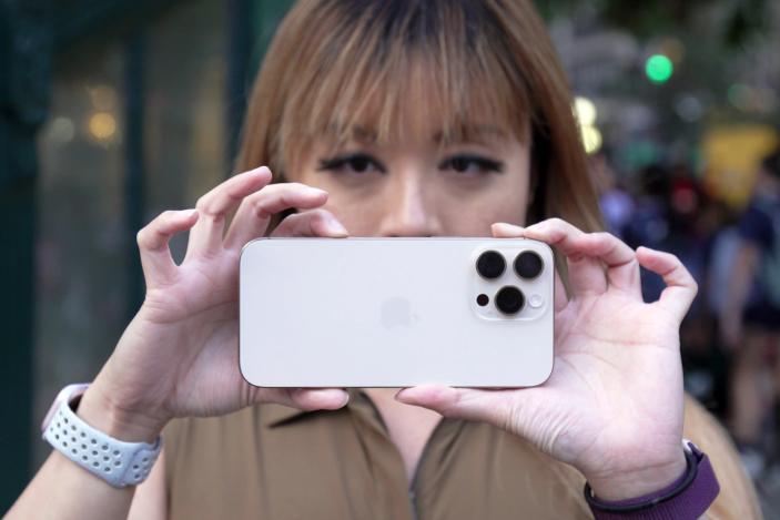 A woman holding the iPhone 16 Pro up in horizontal orientation, with one hand cradling the right side and her other hand positioned with her index finger on the camera control and her thumb at the bottom.