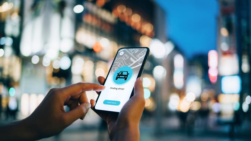 Close up of young woman using mobile app device on smartphone to arrange a taxi ride in downtown city street, with illuminated city traffic scene as background