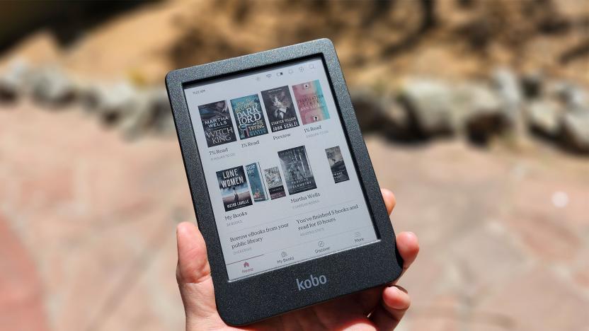 A person holds the Kobo Clara Colour in the sun. The color covers of some books are displayed on the screen. There are rocks in the background. 