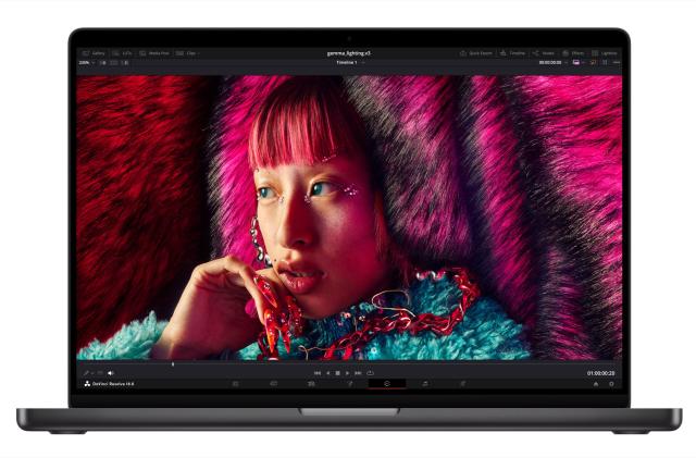 A press photo of the new Apple MacBook Pro powered by the new M3 chip. The dark gray laptop is facing forward with a photo of a young woman with brightly colored hair and a fuzzy blue top on the notebook's display.