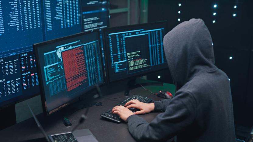 A computer terrorist in a dark hoodie hacks into a computer network, types software code on a keyboard, and monitors a virus attack to hack into government systems and servers. Digital panels with many open windows with program codes and windows for loading digital data.