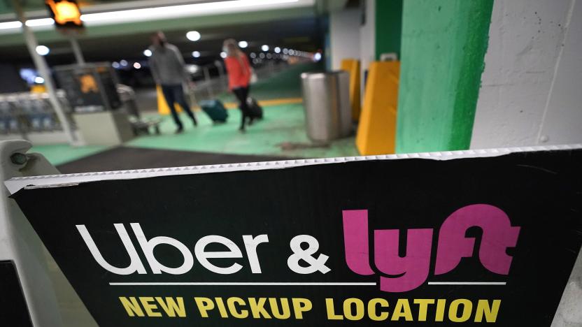 Passers-by pull luggage as they walk near a sign advising travelers of an Uber and Lyft pickup location at Logan International Airport, in Boston, Tuesday, Feb. 9, 2021. (AP Photo/Steven Senne)