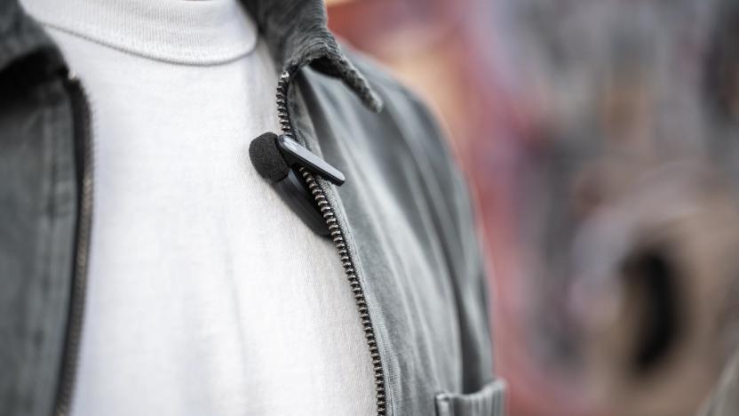 Product lifestyle image for the Shure MoveMic clip-on lavalier microphone. A person has the mic clipped to a gray-colored jacket with light material.