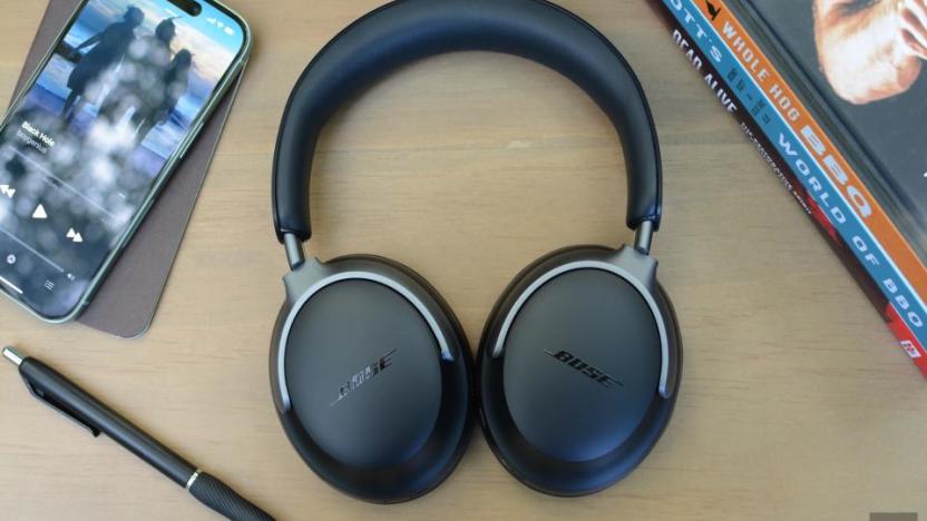 Review photo of the Bose QuietComfort Ultra headphones, sitting on a table next to a pen, phone and books.