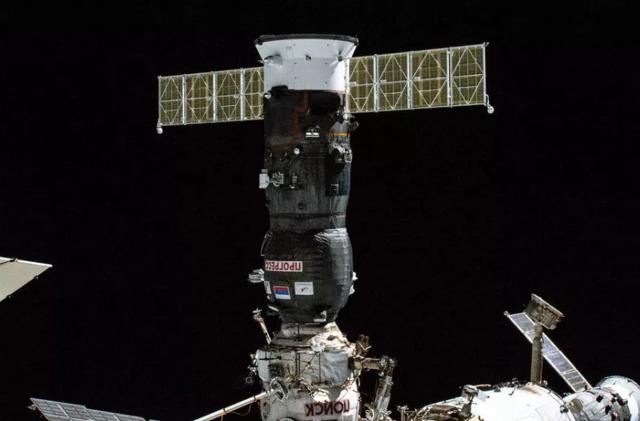 Image of a Russian Progress supply craft docked with the International Space Station, with the black of space in the background.