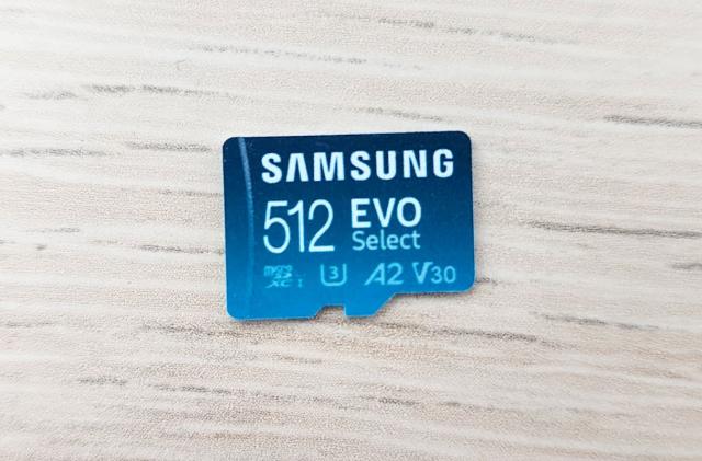 A closeup of a Samsung 512 EVO Select microSD card on a white wood-textured tabletop.