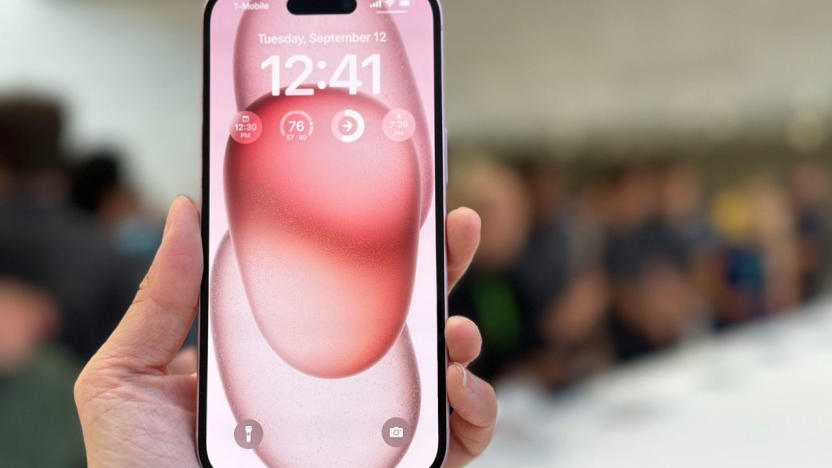 A pink iPhone 15 held in mid-air with its screen facing the camera.  