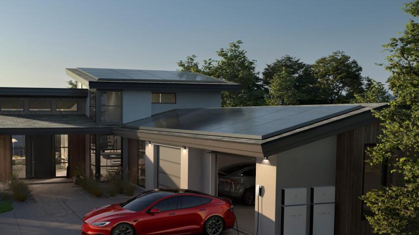 A house with solar panels on the roof. In front of the garage door is a red Tesla plugged into an outlet. White Powerwall units are visible on the outside wall of the garage.