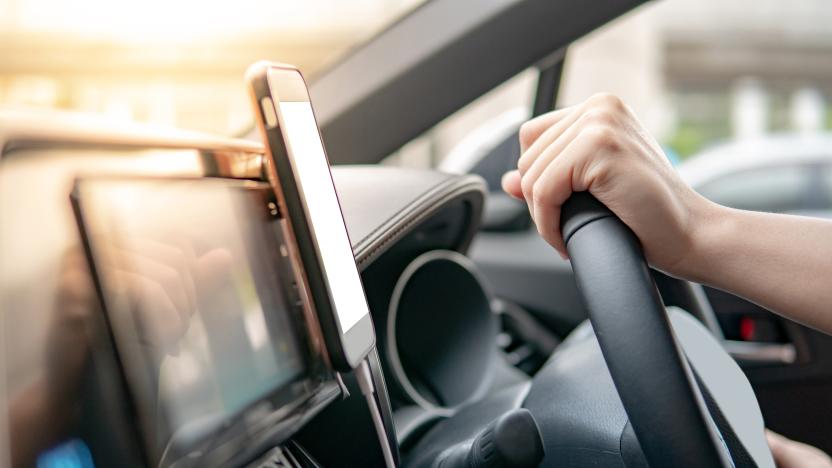 Male driver hand holding on steering wheel using smartphone for GPS navigation. Mobile phone mounting with magnet on the car console in modern car. Urban driving lifestyle with mobile app technology