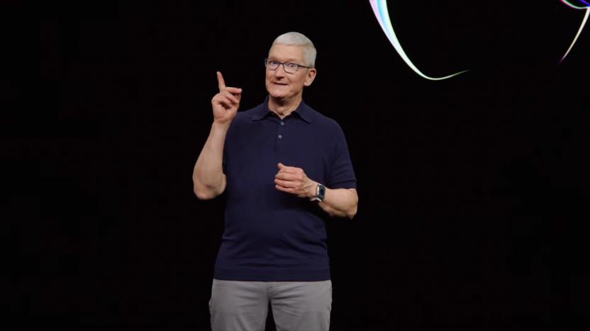 Tim Cook standing in front of a black backdrop (with segment of an Apple logo visible) holding up his index finger