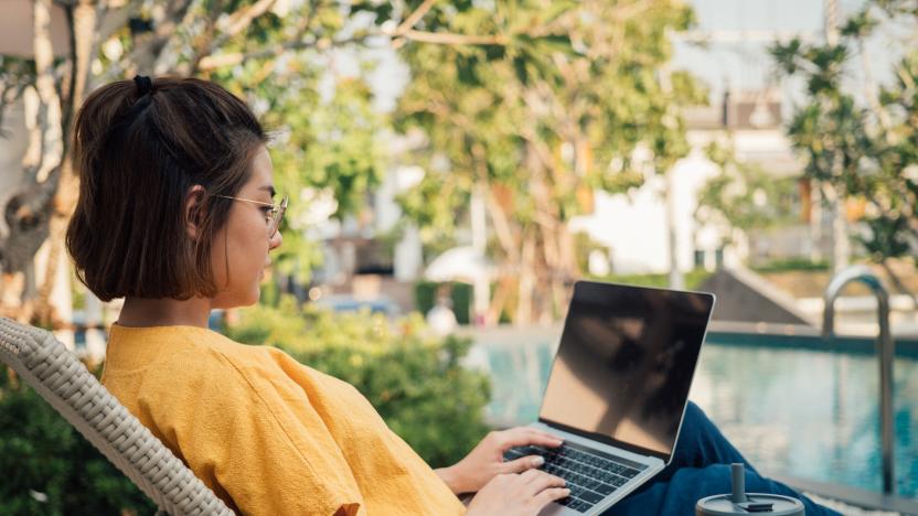 Freelancer working with laptop and smart phone and lying on deck chair near the pool at resort on summer vacation.