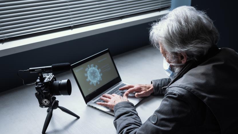 Senior man sitting at desk and wearing a surgical mask, he is connecting with his laptop and streaming a video online on his channel, covid-19 virus outbreak and communication concept