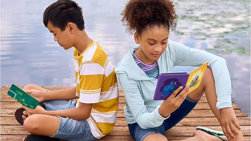 Two kids sitting on a dock with Kindle Paperwhite e-readers encased in colorful cases open in their hands. 