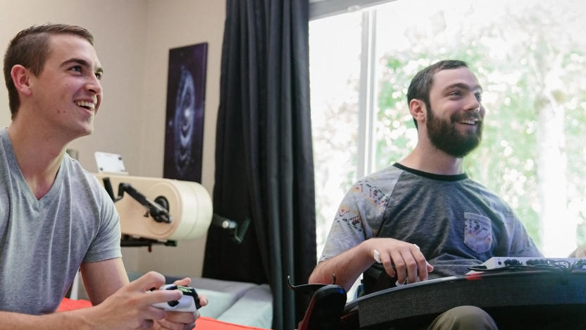 Xbox marketing photo showing two young men playing Xbox games. One of them is using a standard Xbox gamepad, and the other has the Xbox Adaptive Controller.