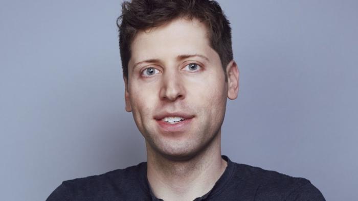 Headshot of OpenAI CEO Sam Altman. He looks into the camera with a partial smile against a grayish background.