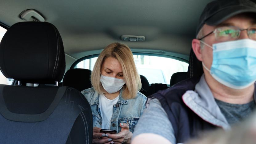 Caucasian woman in taxi wearing face mask for protection from pollution and viruses such as Coronavirus. Using smartphone