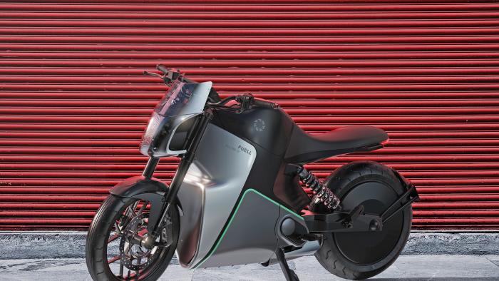 A press photo of Fuell Flloww electric motorcycle seen from the side on a sidewalk in front of a red roll down metal gate.