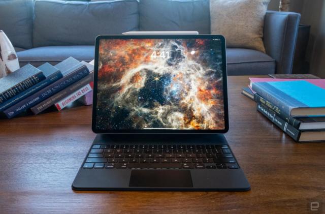 An iPad Pro with a dynamic galaxy wallpaper sitting on a desk with books. A couch looms behind it.