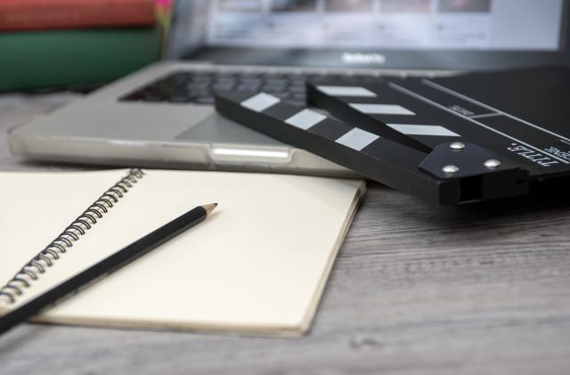 office stuff with Movie clapper laptop and coffee cup pen notepad on the wood table top view shot.dark effect