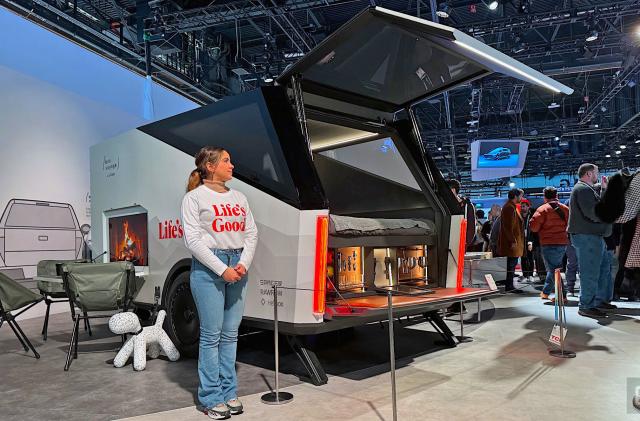 A woman standing next to a high-tech concept trailer from LG at CES 2024. There are camping chairs to the side of the trailer. 