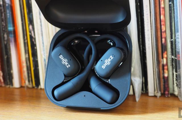 Close-up images of the Shokz OpenFit open-ear buds in grey with the charging case.