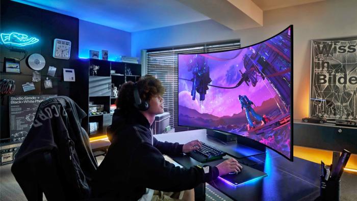 Product lifestyle photo of a young person playing a game on the Samsung 55-inch Odyssey Ark monitor. The enormous monitor curves around his head for an immersive view, as he games on his PC in a stylish modern gaming room.