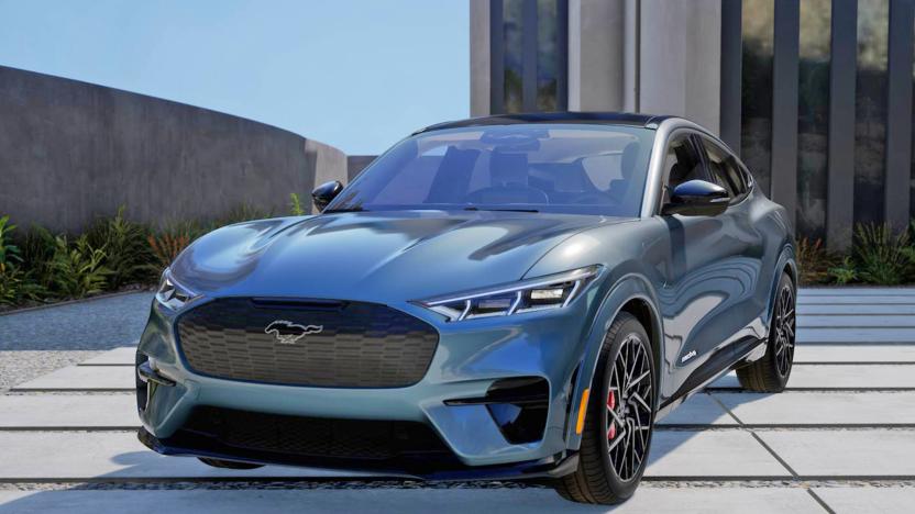 A dark grey 2023 Ford Mustang Mach-E GT Performance is parked outdoors on a lot of modern paving tiles in front of a modern building.