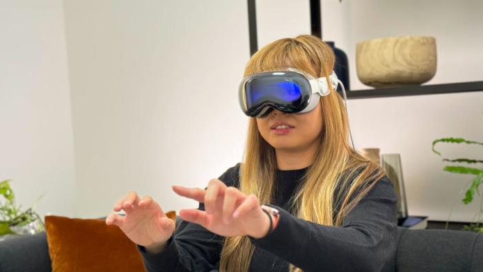 Photo of Engadget’s Cherlynn Low wearing the Apple Vision Pro headset. Her hands are outstretched in front of her as she sits on a modern office couch.