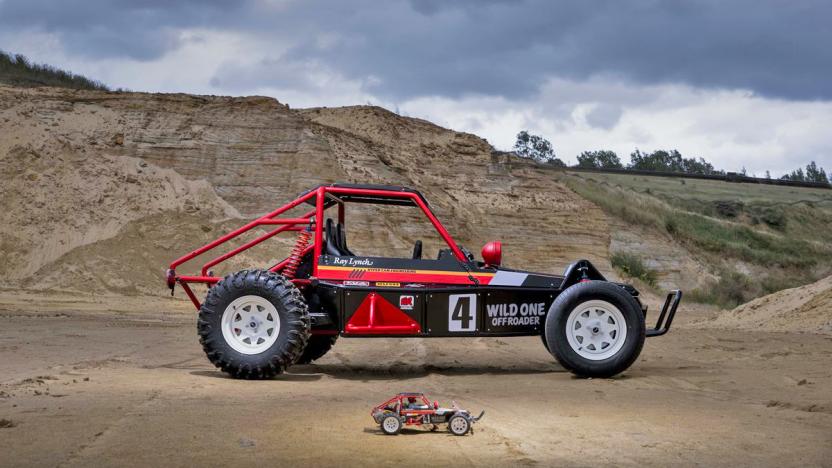 A big off-road Wild One Off Roader rally car style EV is parked behind a small RC version of the same car. 