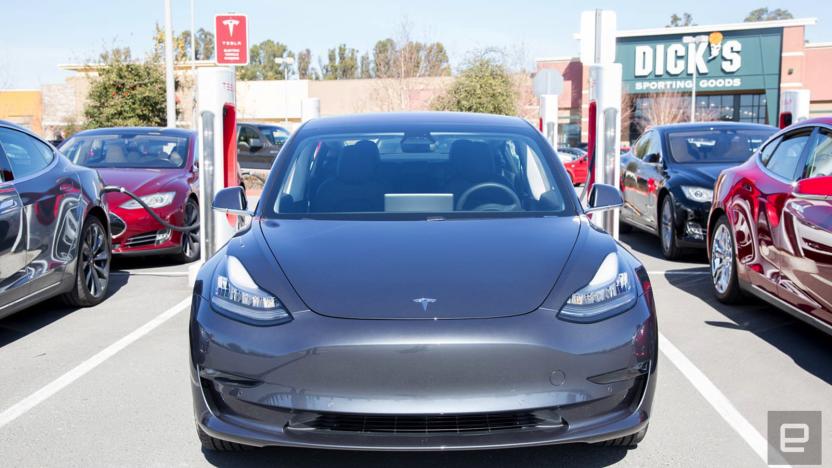 A grey Tesla Model 3 seen from the front as it's parked in a space with a charger.