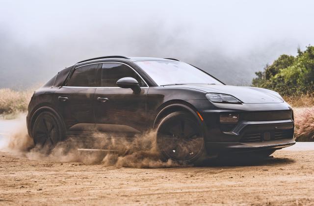 A black Porsche Macan 2025 EV speeds through the dirt shoulder of a road kicking up small dust clouds.