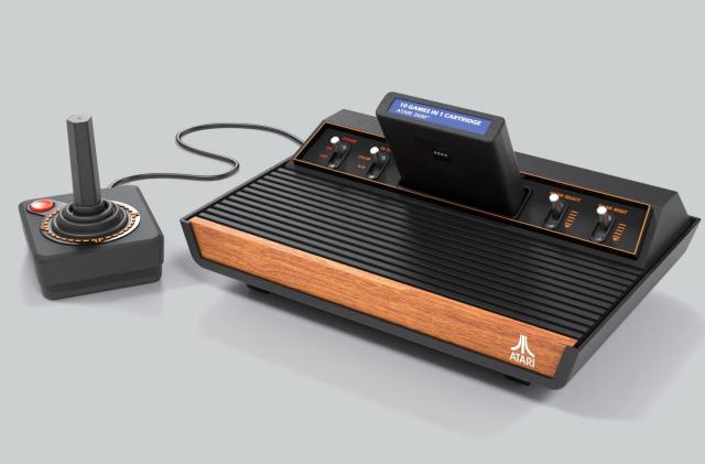 Marketing photo of a new Atari retro console (2600+) that faithfully recreates the look of the original. Vintage-looking console with front wood panel, switches and a companion joystick.