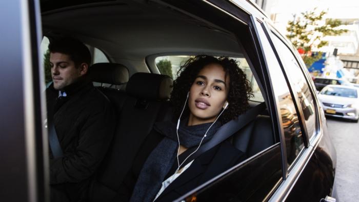 Two Uber passengers listen to headphones as they sit in the back of a black car in NYC.