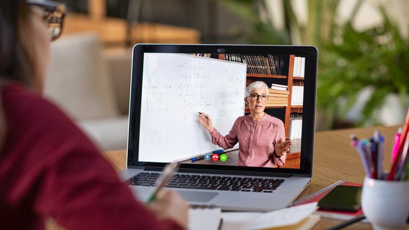 Young student watching lesson online and studying from home. Young woman taking notes while looking at computer screen following professor doing math on video call. Latin girl student studying from home and watching teacher explaining math formula on video chat.