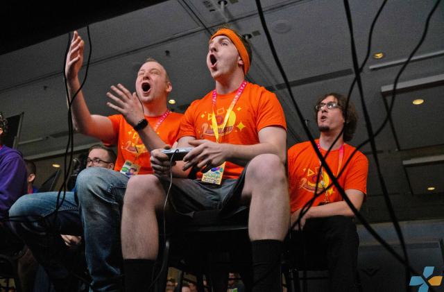 Photo from Summer Games Done Quick 2019, featuring gamers sitting side-by-side, holding controllers and staring intently while appearing to shout or vocalize feelings about the game.