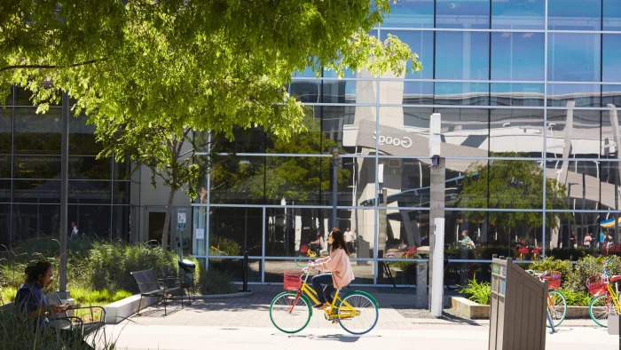 A  person riding a bike in front of a building with a mirror facade.