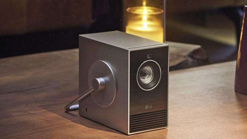 The LG CineBeam Qube projector on a wood table with a candle behind it. 