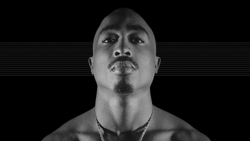 Photo of the late Tupac Shakur, staring down at the camera against a black background with subtle horizontal gray lines.