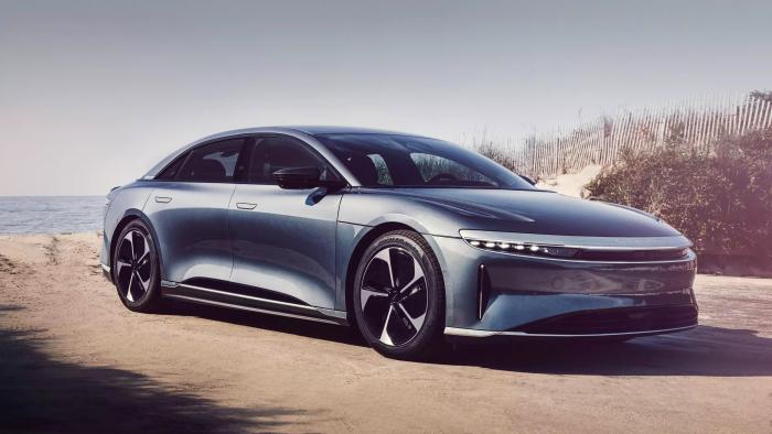 A grey Lucid Air Pure RWD EV is parked among sand dunes on the edge of the beach.