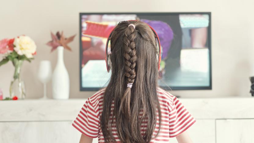 Rear view of little girl with headphones watching television