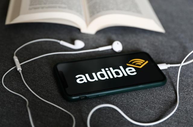 Audible logo displayed on a phone, headphones and a book are seen in this illustration photo taken in Krakow, Poland on August 22, 2022. (Photo by Jakub Porzycki/NurPhoto via Getty Images)