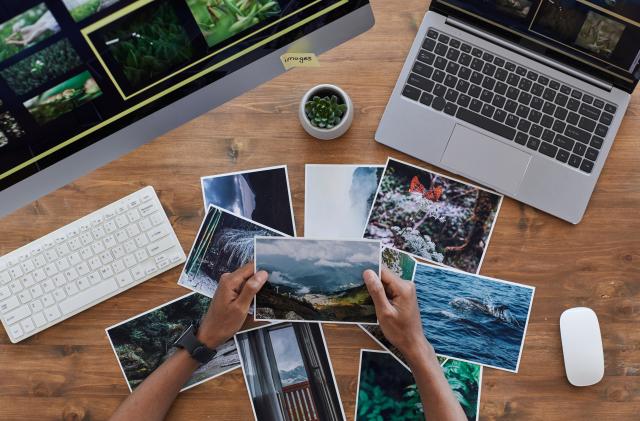 Minimal background composition of male hands holding printed photographs over textured wooden desk, photographers office concept, copy space