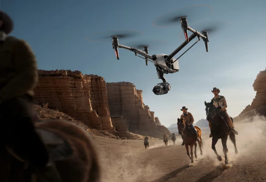 Outdoor Southwest US view (mesas visible in the background) of the drone hovering in the foreground, filming cowboys riding horses.