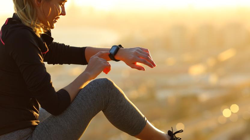 Runner sitting on the ground checking smartwatch after running at sunset