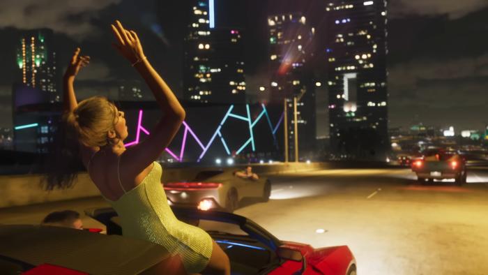 Still from the GTA 6 trailer, featuring a woman holding her hands up and standing in a speeding convertible. Nighttime in Vice City (Miami).