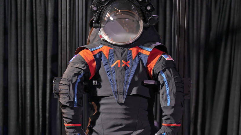 The Axiom Space AxEMU spacesuit for Artemis III Moon mission is presented against a black curtain. The suit is helmeted and mostly dark grey with blue and orange accents.