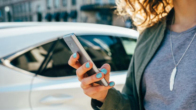 Young woman using smart phone standing on street near road and car. Female's hands holding mobile device in city, close-up.