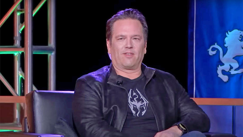 Xbox's Phil Spencer is shown sitting down on stage at an event. The photo is closely cropped so you only see him and the edges of his black chair.