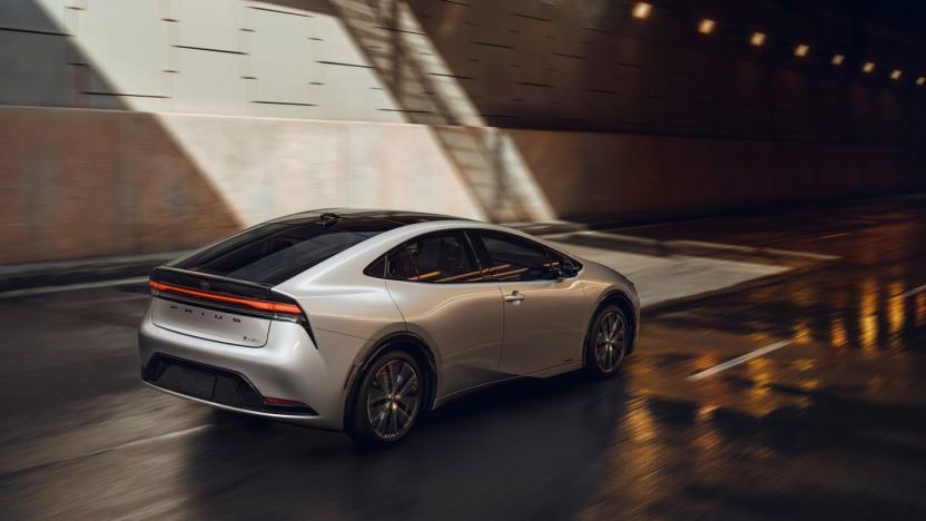 A silver Toyota Prius (2023) drives through an rain-slicked roadway under the shadows of an overpass.