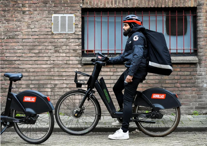 A courier of the fast grocery deliverer Gorillas sits on a bike as Amsterdam and Rotterdam have moved to ban new "dark store" delivery hubs in the city centres, in Rotterdam, Netherlands February 8, 2022. Picture taken February 8, 2022. REUTERS/Piroschka van de Wouw